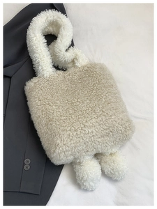 Détail du sac fourre-tout crème en peluche avec pompons sur un blazer gris