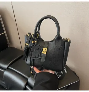 Close-up of black lychee grain leather bucket bag featuring gold buckle and dog charm