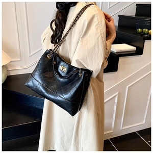 Detail of black quilted tote bag featuring gold chain strap and metal twist lock closure