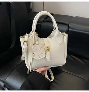 Close-up of cream leather bucket bag featuring lychee texture and a cute dog charm