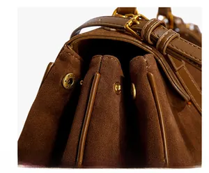 Detail view of brown matte suede shoulder bag with accordion sides and gold buckle