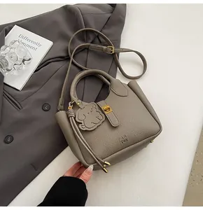 Detail of grey lychee pattern leather handbag with bear charm on a dark blazer