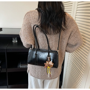Détail du sac baguette noir brillant avec charm ours mignon sur la bandoulière