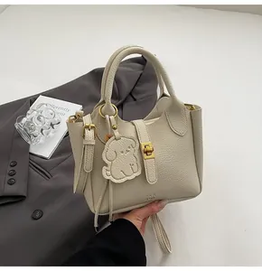 Detail of beige litchi grain bucket bag with cute dog charm and gold hardware clasp