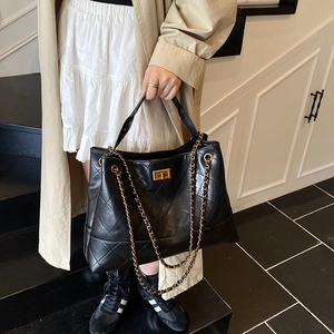 Quilted black leather tote bag with gold chain strap shown on person in trench coat