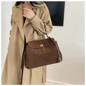 Detail of dark brown matte leather shoulder bag with golden twist-lock closure on model