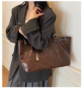 Detail of dark brown vintage tote bag with silver eyelets and buckle accents on model
