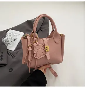 Detailed close-up of pink litchi grain leather bucket bag with dog pendant and gold metal hardware