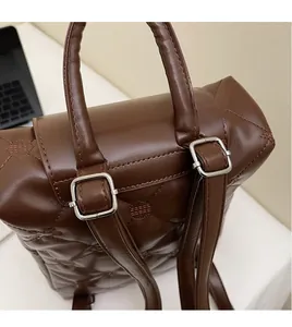 Detail of dark brown quilted leather backpack showing top handle and adjustable straps
