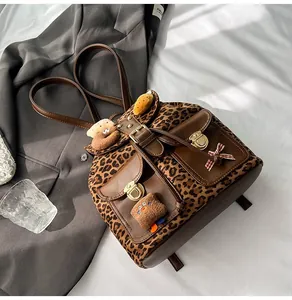 Close-up of leopard print backpack with brown leather lid, gold buckles and plush charms