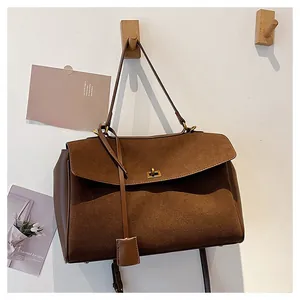Détail du sac cabas en daim marron avec fermoir rotatif doré sur un crochet en bois