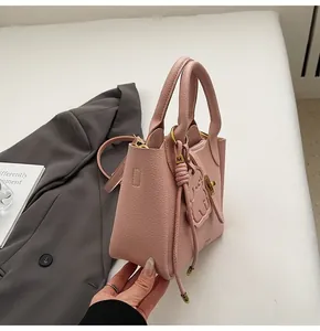 Detail of pink lychee leather handbag with gold cat charm and sleek metal hardware