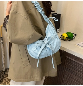 Detail of light blue crossbody bag featuring pleated strap and a large bow tie decoration
