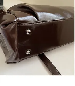 Close-up of dark brown glossy shoulder bag base with silver studs and fine stitching