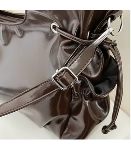 Detail view of dark coffee glossy shoulder bag featuring smooth adjustable long strap