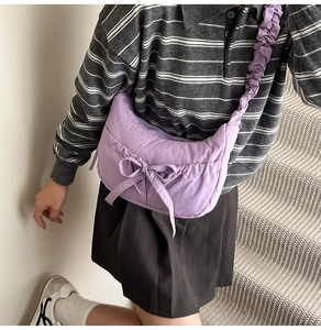 Detail of purple crossbody bag featuring a large decorative bow and pleated shoulder strap