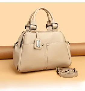 Detail of beige litchi grain cowhide Boston bag with dual handles and metal tag