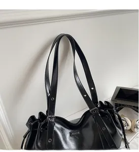 Detail of black glossy shoulder bag with drawstring closure and metal logo plaque