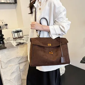 Détail d'un grand sac cabas en daim marron foncé avec fermoir doré et charme en cuir