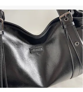 Close-up of black leather shoulder bag showing glossy texture and metallic buckle details