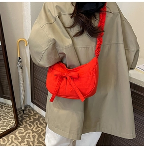 Detail of orange crescent bag featuring a large bow and pleated shoulder strap design