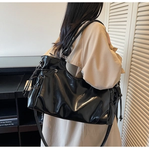 Model wearing a large black glossy tote bag with drawstring detail and a long strap