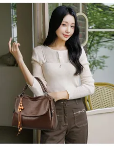 Detail of brown leather tote bag featuring side zipper and wooden beaded tassel charm