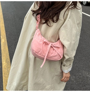 Detailed view of pink pleated nylon crossbody bag with bow accent and drawstring strap