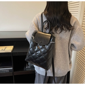 Rear view of model wearing a black quilted leather backpack with elegant floral embroidery