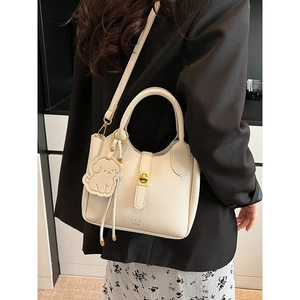 Chic beige lychee leather bucket bag with top handle and gold hardware shown on a model