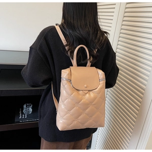 Detailed back view of a beige quilted diamond pattern backpack on a model in a cozy interior