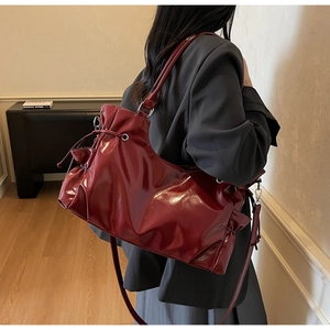 Deep red patent leather tote bag with drawstring closure shown on shoulder in lifestyle scene