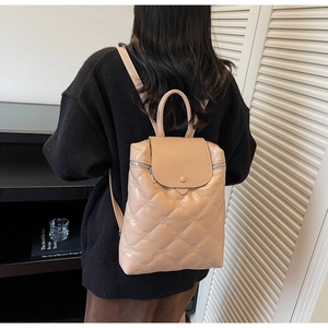 Quilted beige backpack with flower embroidery and silver zippers on model's back