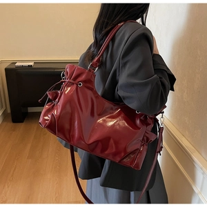 Detail view of burgundy glossy crossbody bag featuring drawstring closure and metallic rings