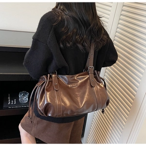 Détail du sac cabas marron foncé avec logo métallique et bandoulière réglable sur modèle