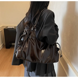 Detail of a large dark brown patent leather tote bag with a drawstring closure