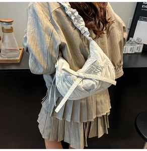 Detail of white pleated crescent bag with bow decoration on model in a cafe
