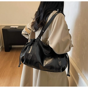 Detail of a black glossy shoulder tote bag with drawstring closure on a beige coat
