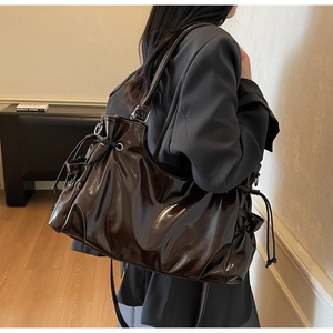 Close-up of glossy patent leather tote bag with drawstring side details on a model