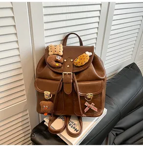 Brown PU leather backpack detail with cartoon plush charms and red checkered bow decoration