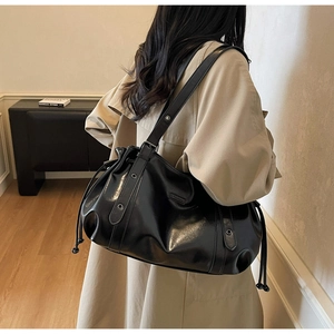 Détail du sac cabas en cuir noir brillant avec cordon sur un trench-coat beige