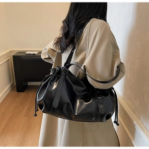 Model wearing a black ruched shoulder bag with metallic eyelet strap detail