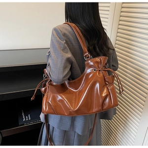 Brown glossy leather tote bag with drawstring closure shown on shoulder of a model