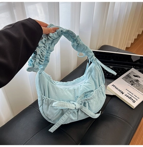 Detail of light blue nylon pleated bag featuring large decorative bow and ruffled handle