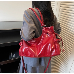 Red glossy leather tote bag with drawstring closure worn over a grey oversized blazer