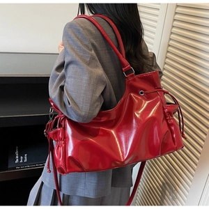 Glossy red patent leather shoulder bag with drawstring detail shown on a model