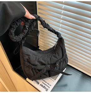 Detail of black pleated nylon shoulder bag with bow and ruffled strap in natural light
