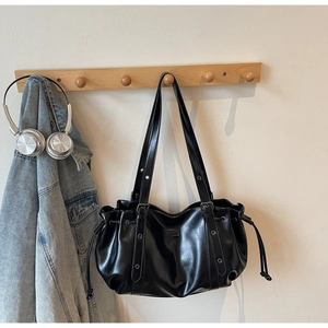 Détail du sac à bandoulière en similicuir noir avec œillets métalliques et cordon de serrage