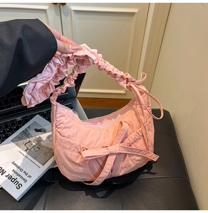 Detail of pink pleated nylon crescent bag featuring soft bow and textured shoulder strap