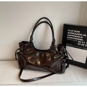 Detail of dark brown tote bag in glossy patent leather with side drawstrings and strap